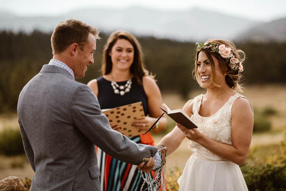 Bride reads vows to groom during intimate elopement ceremony in Rocky Mountain National Park, Colorado. She is wearing a flower crows with pink roses, and a white dress. 