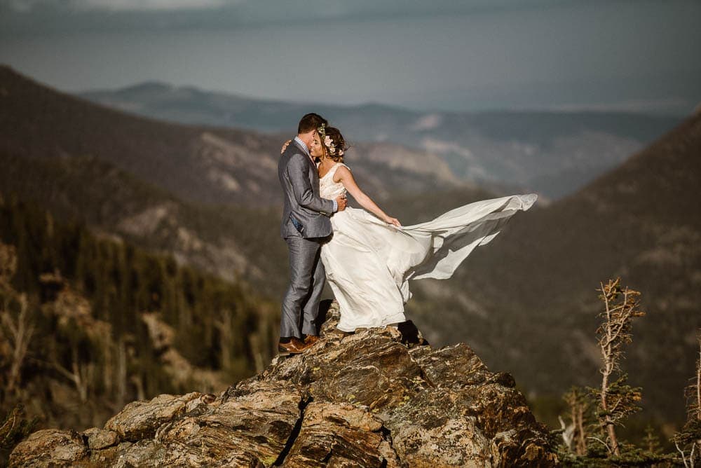 Bride and groom embrace, while bride's dress flows in the wind. There are mountains behind them in Rocky Mountain National Park. 