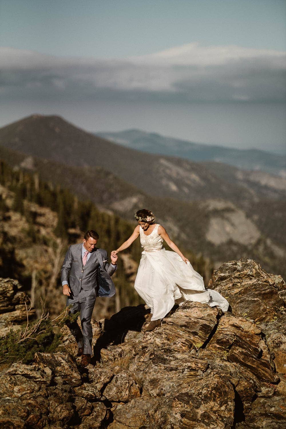 Bride and groom walk on mountain in Rocky Mountain National Park while holding hands. 