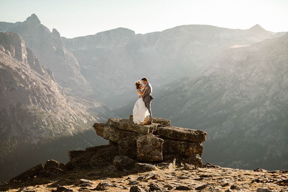 Bride and groom embrace on rocks, with mountains behind them, in Rocky Mountain National Park, Colorado. 