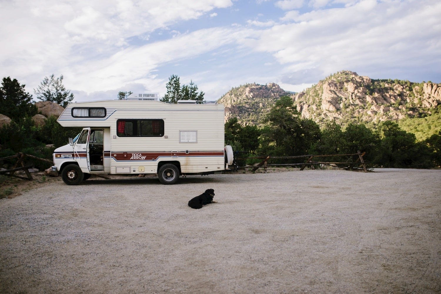 Dog resting on gravel road in front of RV, with mountains in the background, in Buena Vista, Colorado.