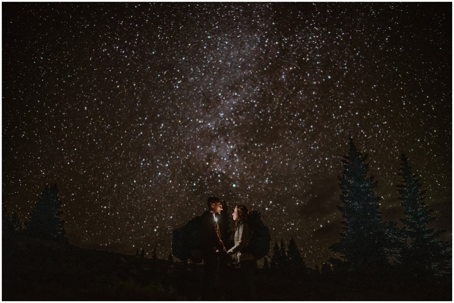 Bride and groom facing each other and holding hands, while wearing headlamps in the dark. Stars and trees visible behind them in Buena Vista, Colorado. 