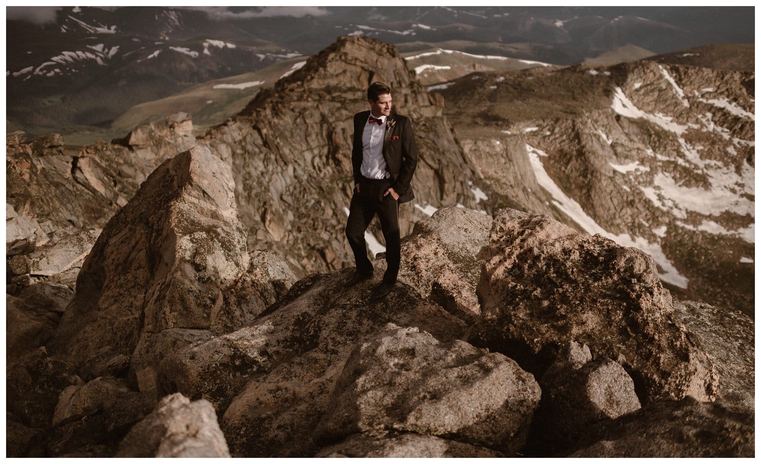 Groom standing on the top of a mountain. He is wearing a black suit. 