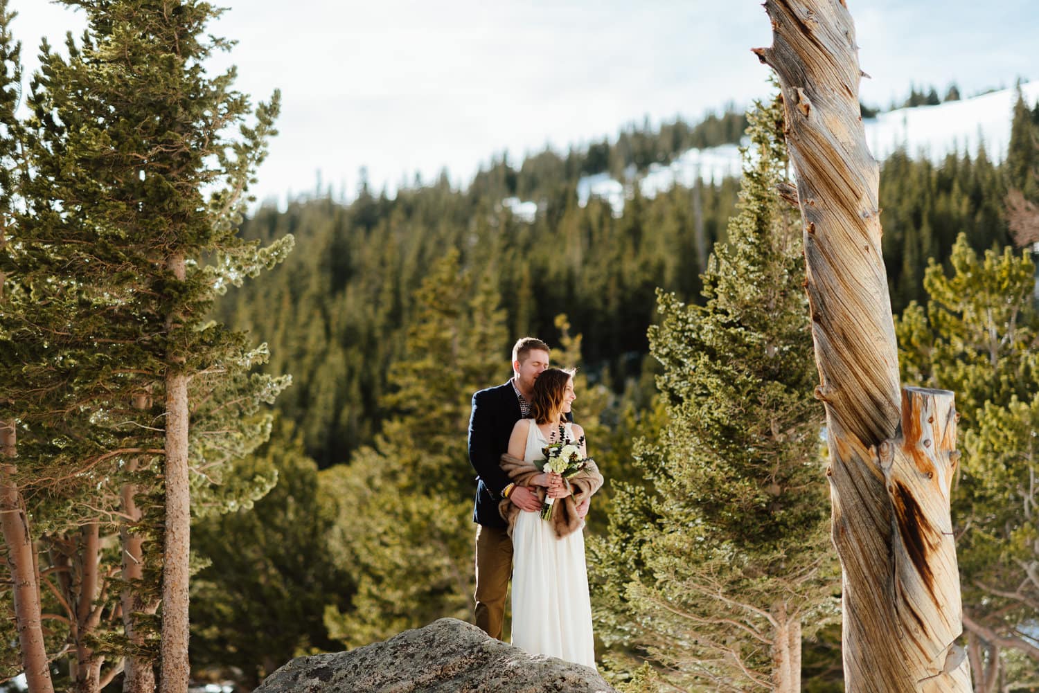 Bride and groom embrace while standing on a rock together at St. Mary's Glacier in Idaho Springs, Colorado. 