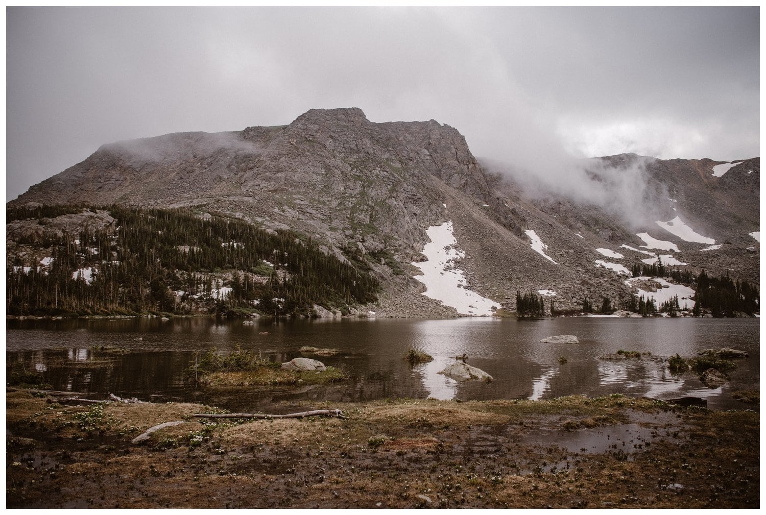 Landscape of a cloudy, grey sky over mountains and a high alpine lake near Boulder, Colorado.