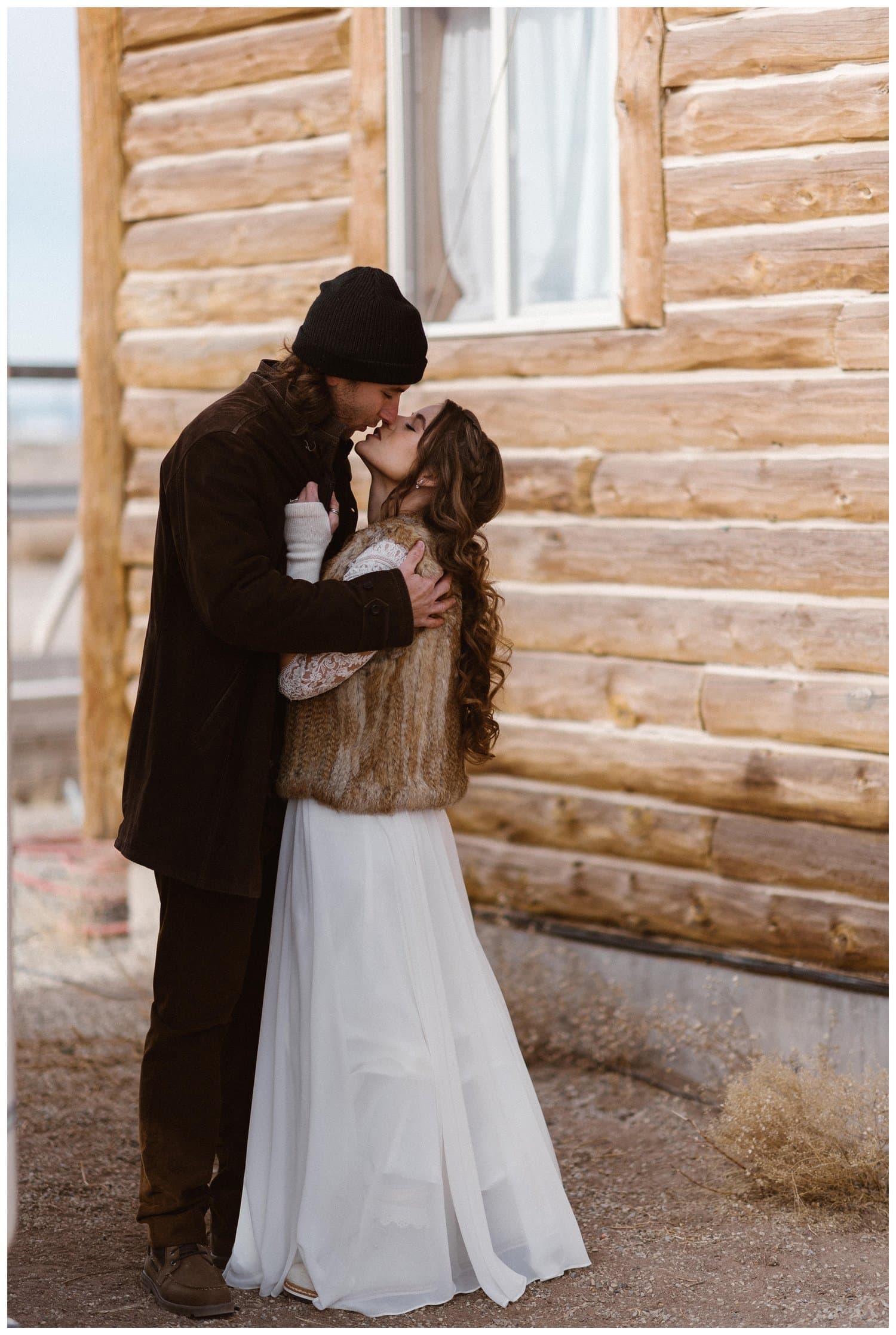 Bride and groom embrace in front of cabin. 