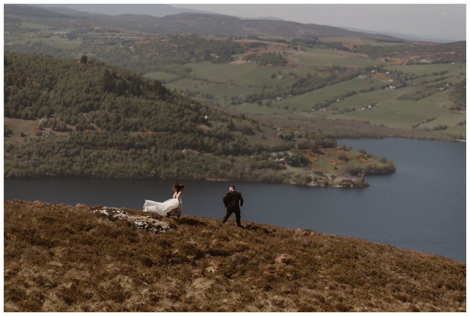 Bride and groom run along a ridge overlooking Loch Ness in the Scottish Highlands. 