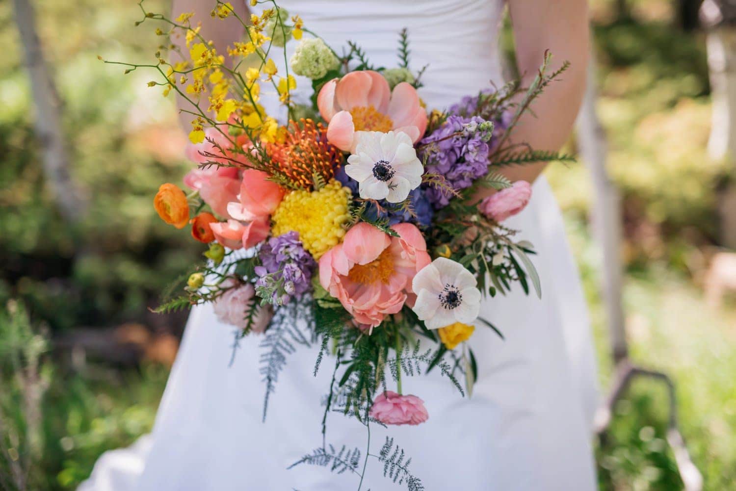Close-up bride holding a bouquet. The flowers are a variety of light pink, purple yellow, orange, and white.