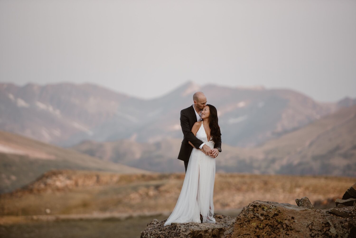 Bride and groom embrace on a mountain top.