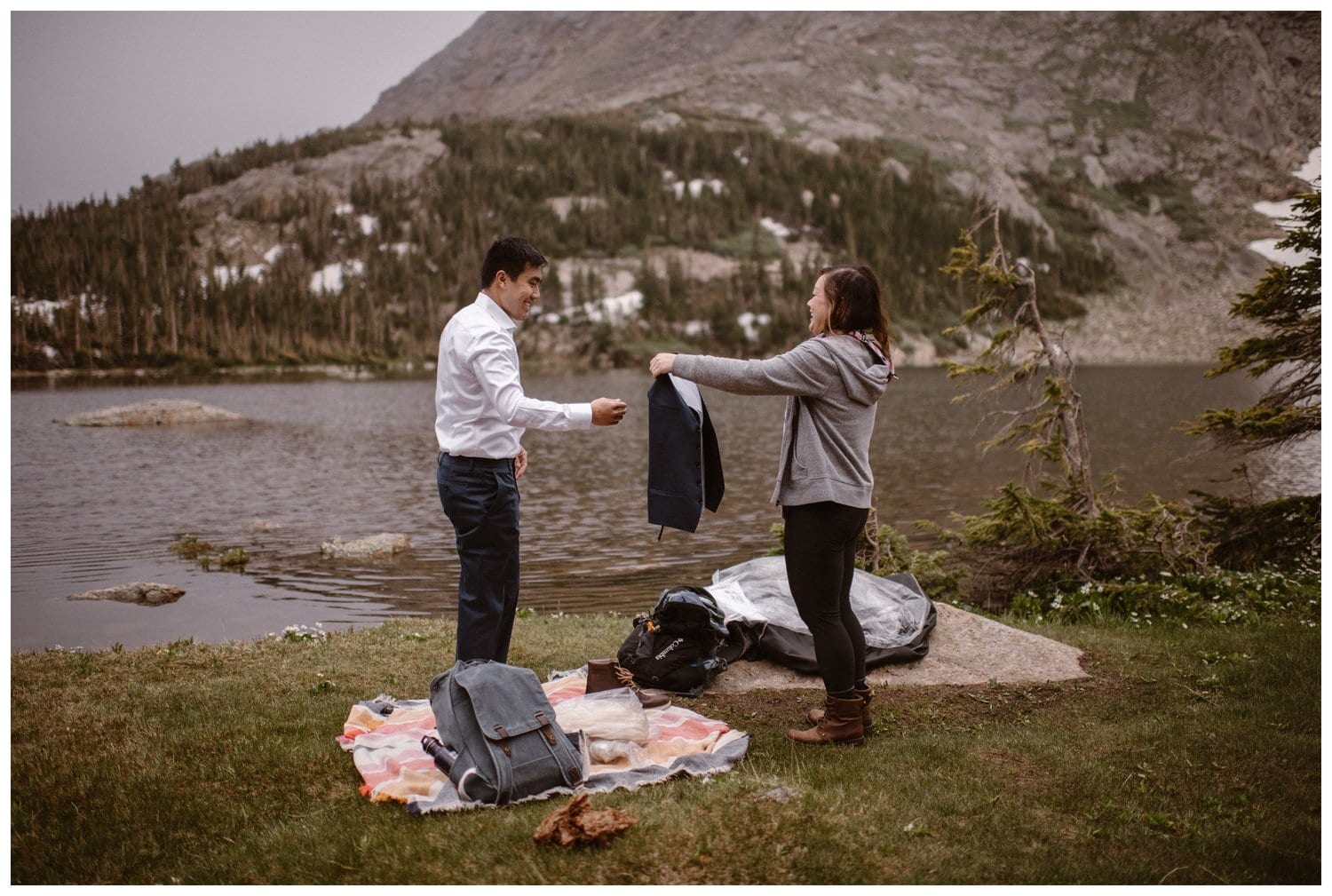 Bride helps groom get dressed in front of a high alpine lake near Boulder, Colorado. 