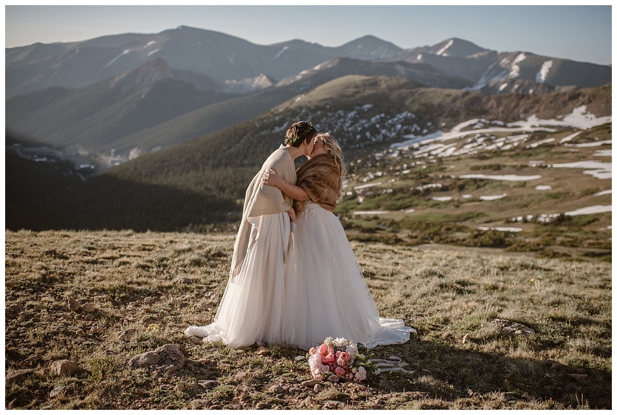 Two brides kiss with mountains in the background in Winter Park, Colorado. 