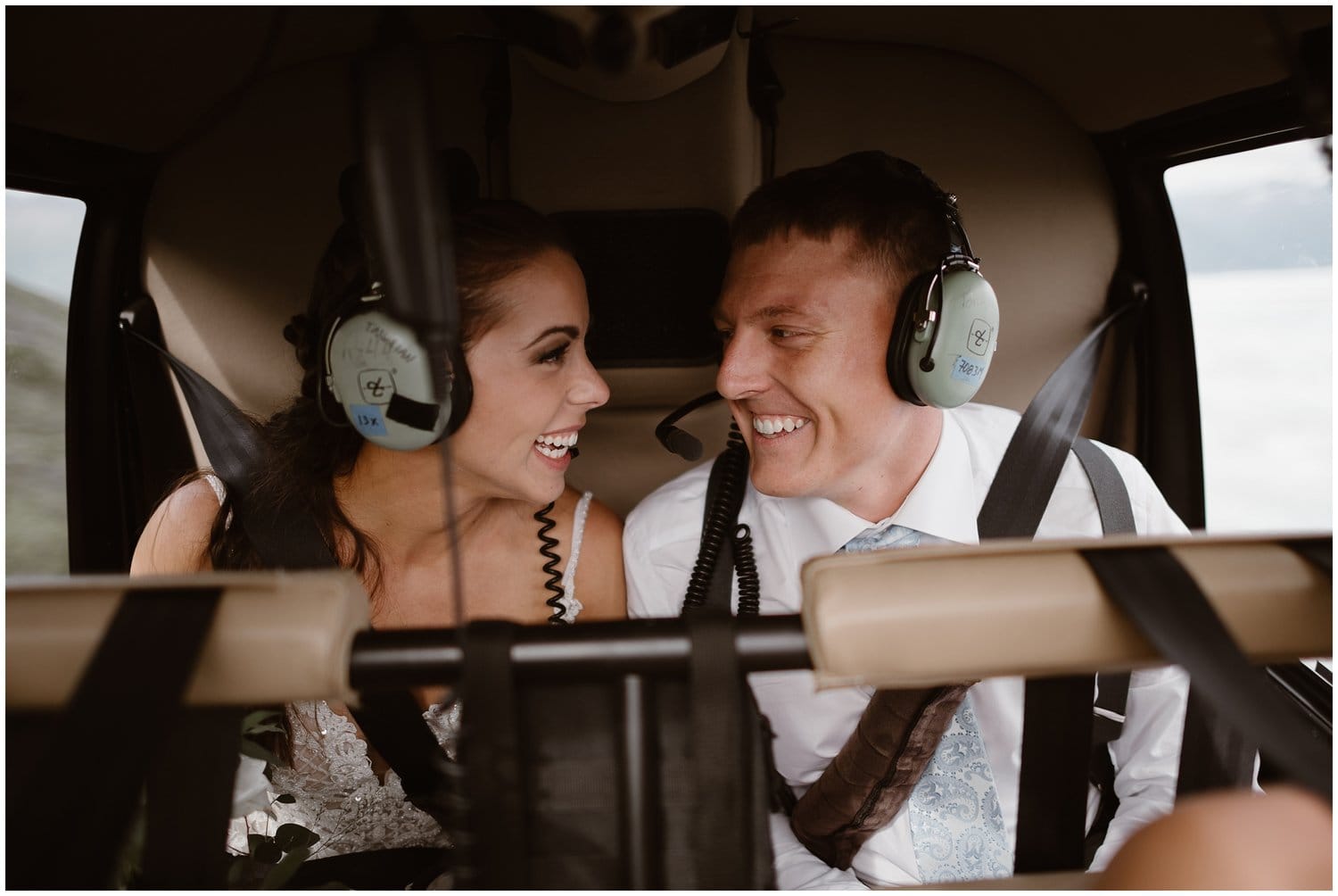 Bride and groom smiling at each other while riding in a helicopter, during an all-day elopement in Alaska. 