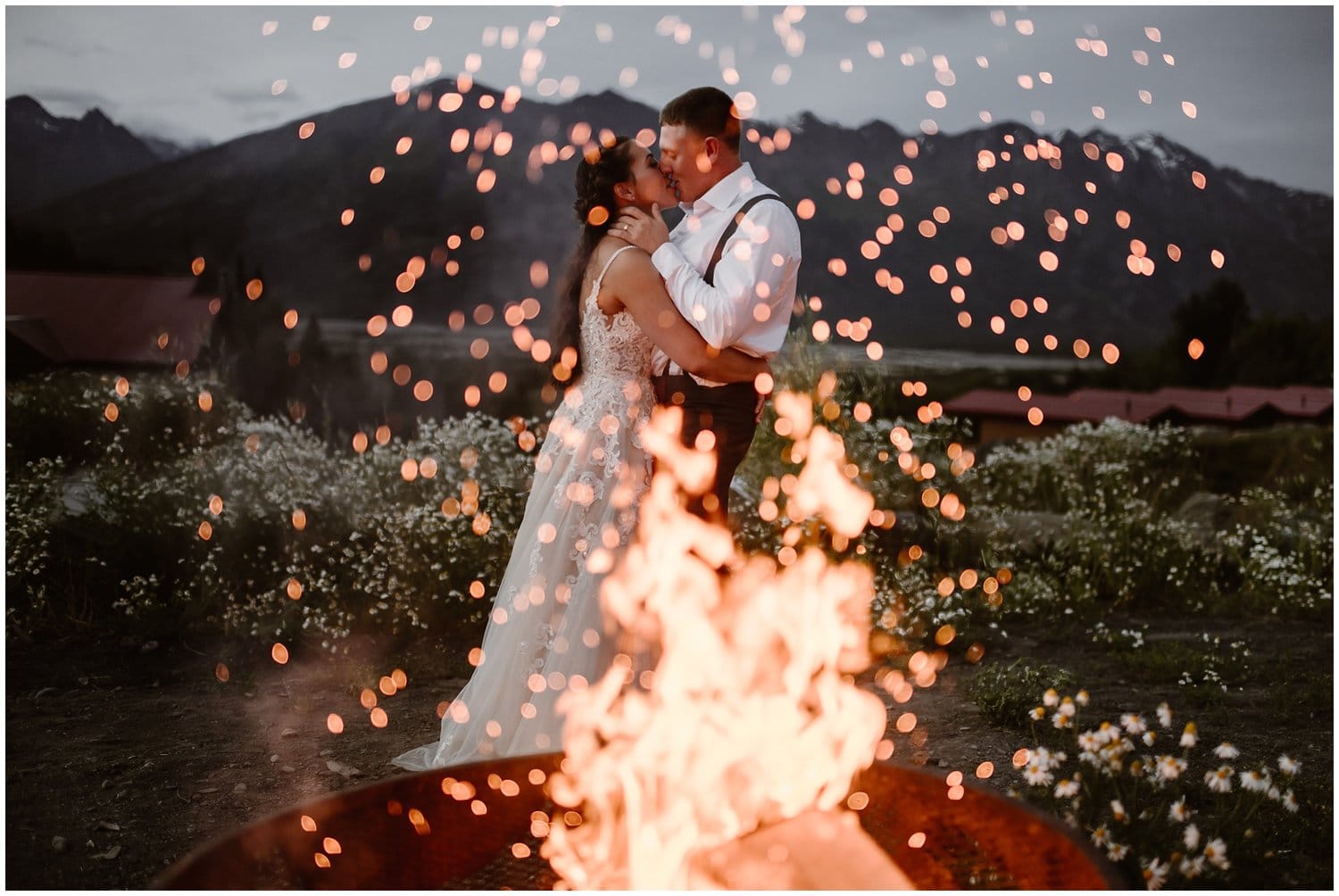 Bride and groom share a kiss, with a bonfire in the foreground, during their all-day elopement in Alaska. 
