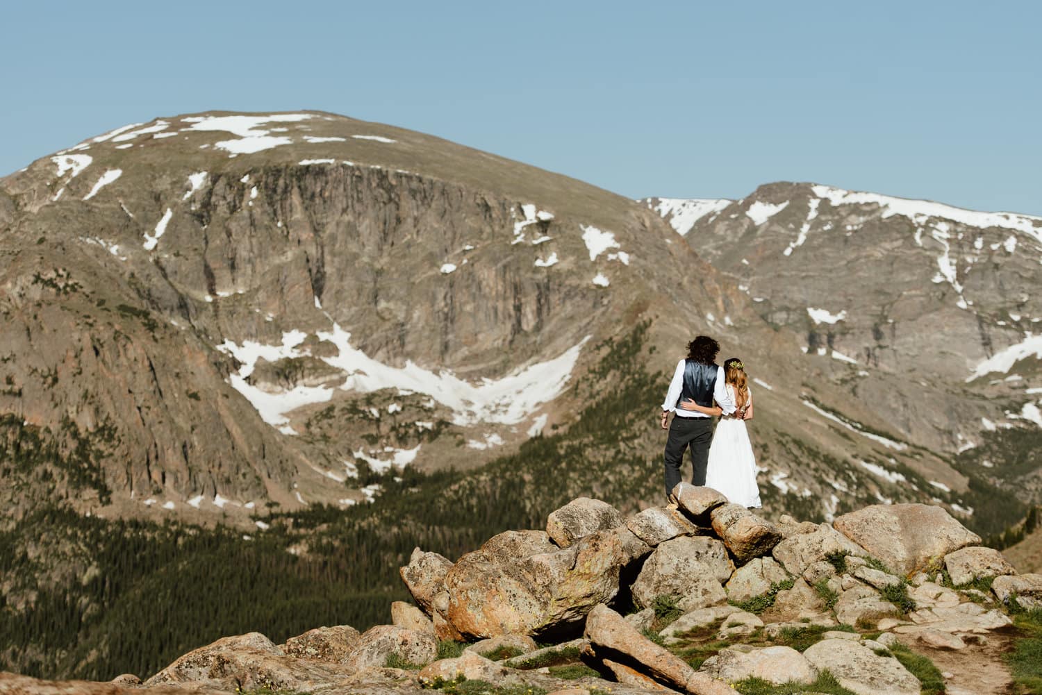 Bride and groom wrap their arms around each other while looking out at the mountains at Trail Ridge Road in Rocky Mountain National Park, Colorado. 