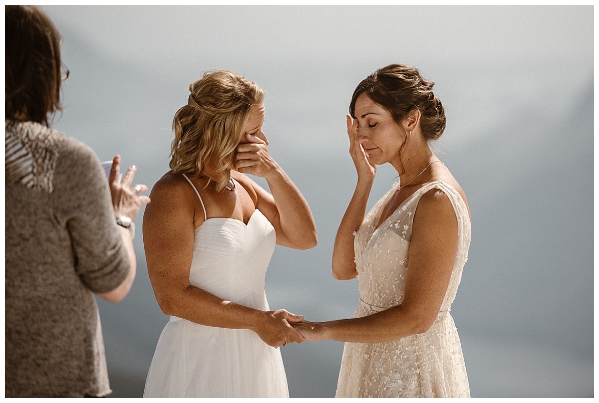Two brides hold hands and wipe away tears during their intimate elopement ceremony on glacial mountain in Tofino, Canada. 