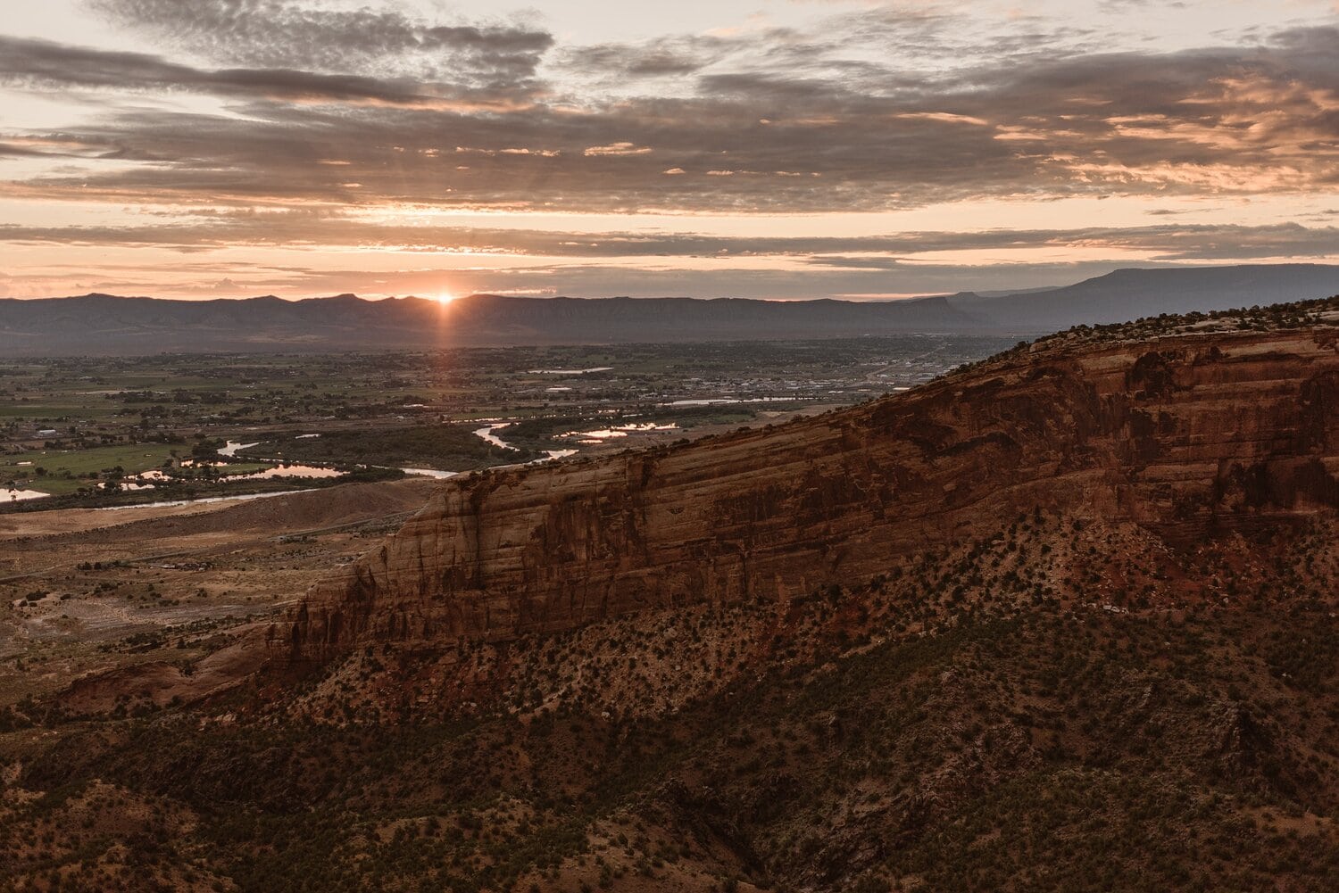 Landscape of mountain range and sunrise at Colorado National Monument. Red rocks in foreground. 