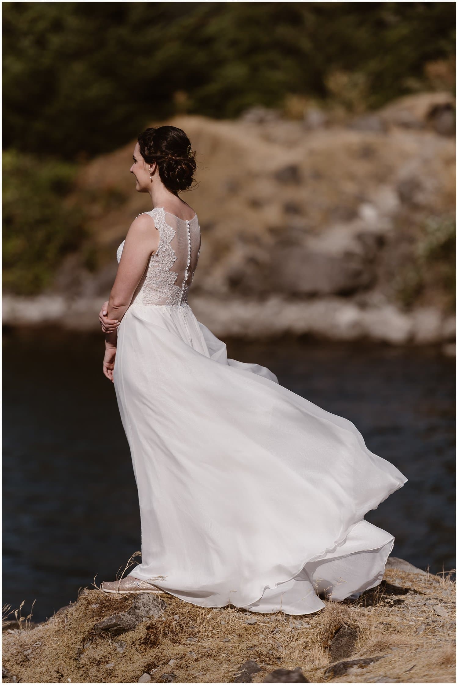 Bride standing on a cliffside, with the Oregon Coast in front of her. She has her hair in an updo and is wearing a white dress that is flowing behind her. 
