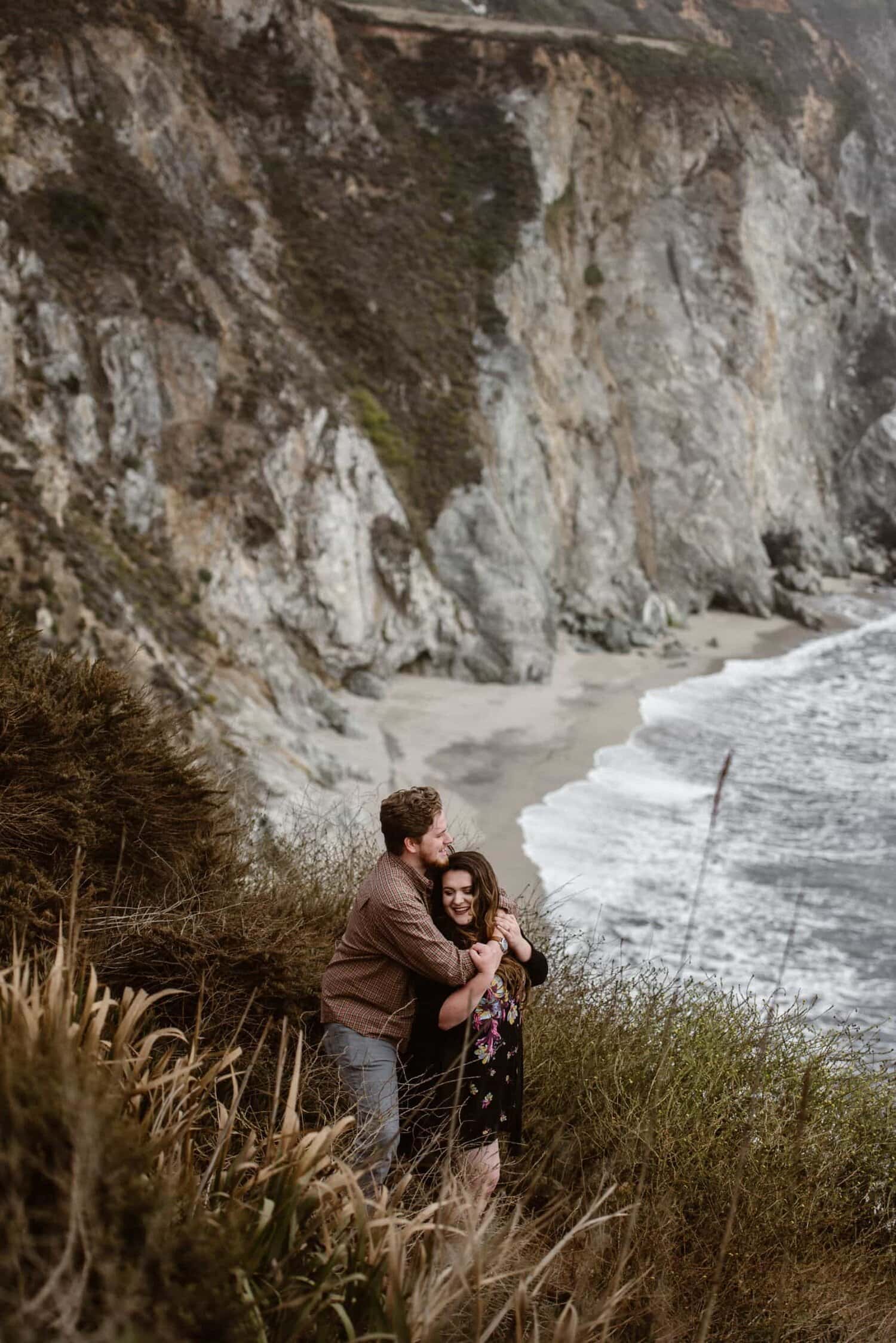 Bride and groom embrace surrounded by tall grass, with the ocean in the background in Big Sur, California.