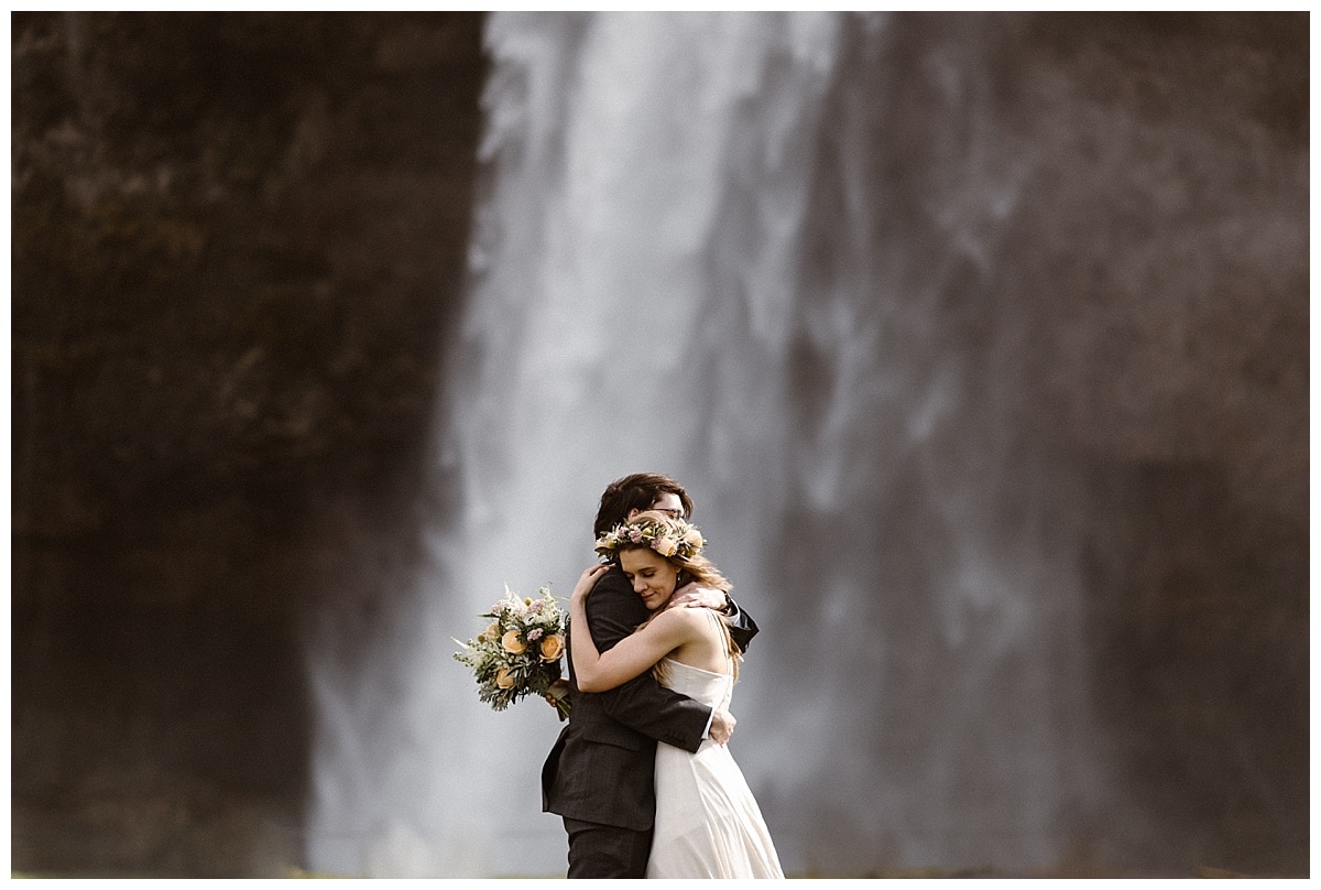 Bride and groom embrace in front of a waterfall in Iceland. 