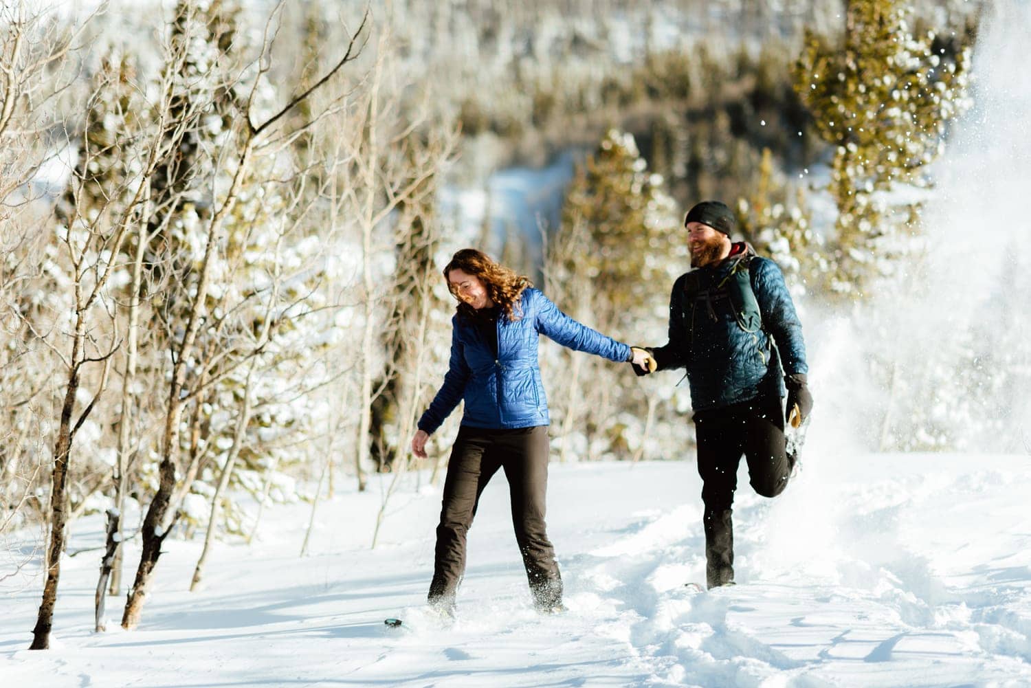 Couple holding hands while snowshoeing at Indian Peaks, in Colorado. There is snow covering the ground and a forest with snow-covered trees in the background. 