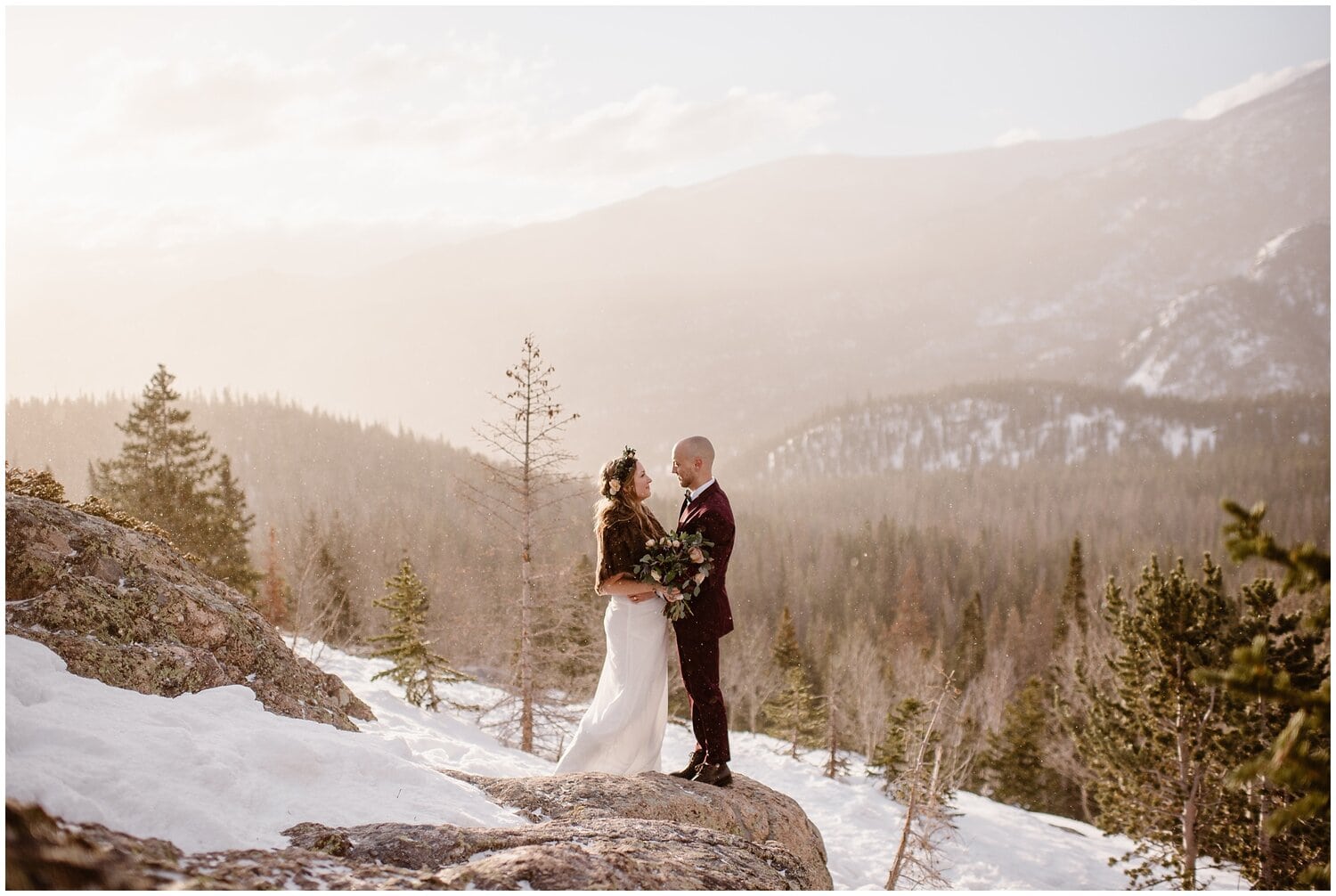 Bride and groom look into each others eyes, surrounded by snow, trees, and mountains. 