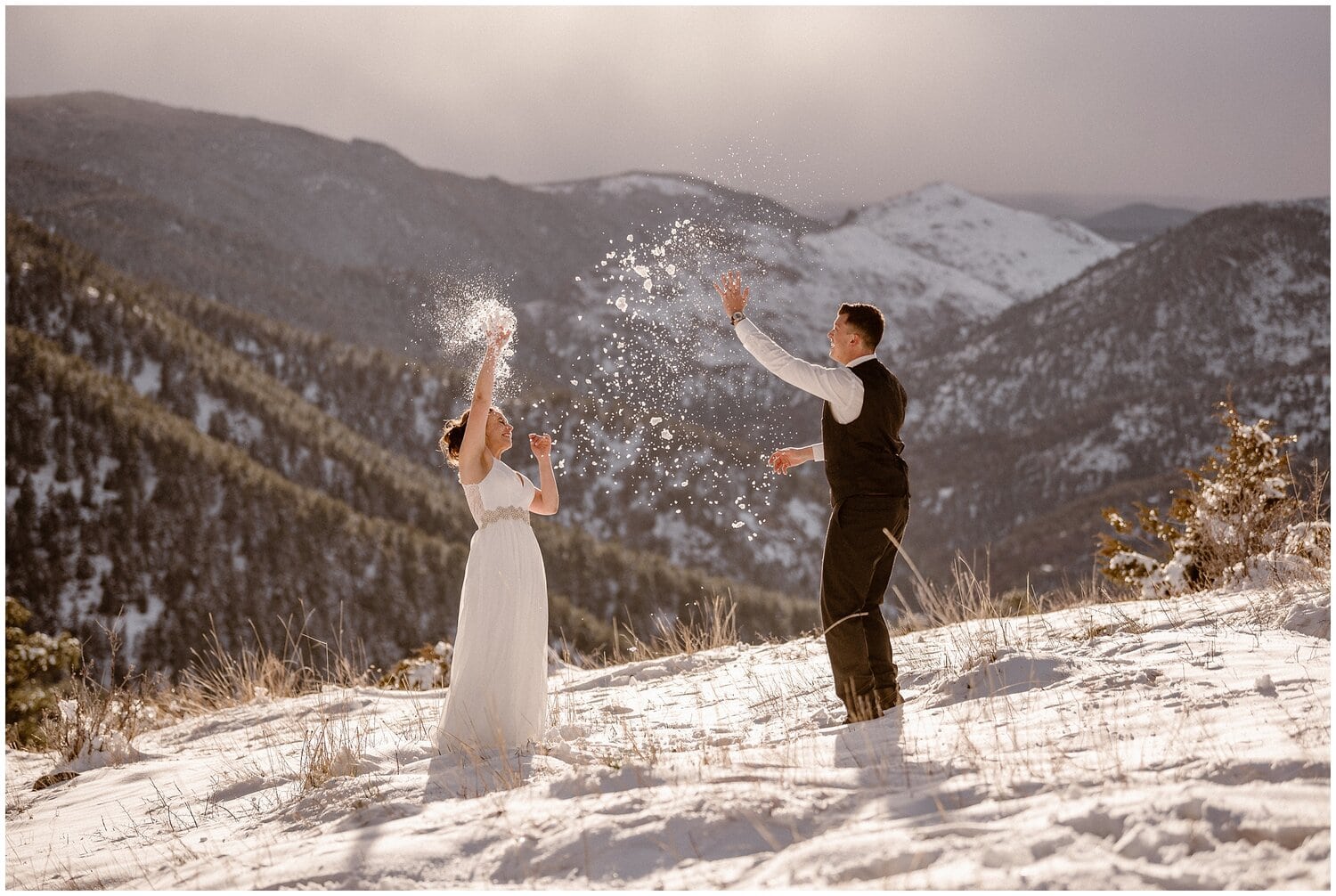 Bride and groom throw snow in the air while laughing. 