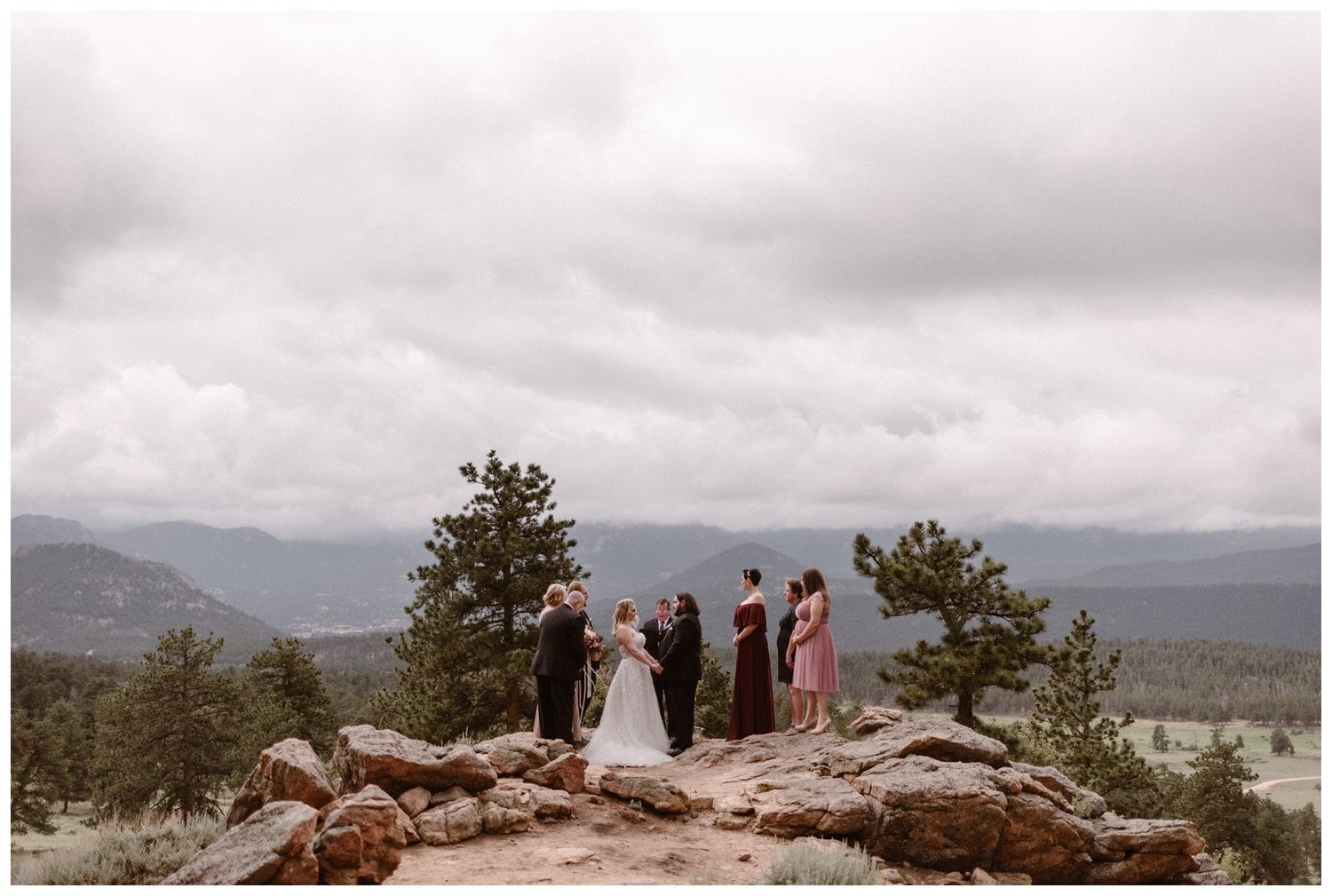 Bride and groom hold hands, surrounded by friends and family, during their elopement ceremony at 3M Curve in Rocky Mountain National Park, Colorado. 