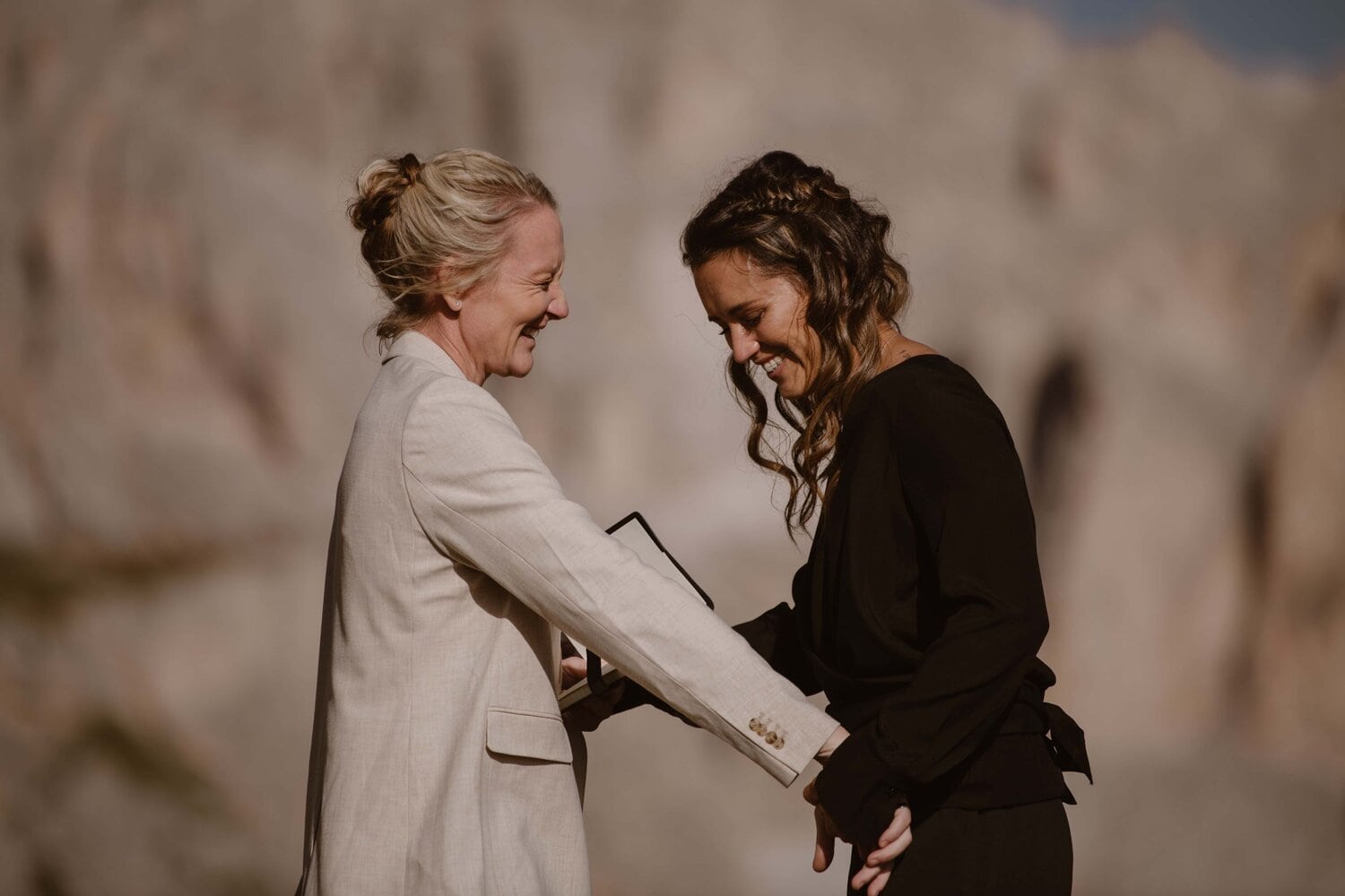 Two brides laughing while holding hands in the Italian Dolomites.