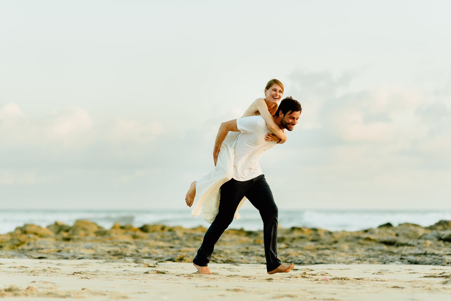 Groom gives bride a piggyback ride on the beach in Santa Teresa, Costa Rica.