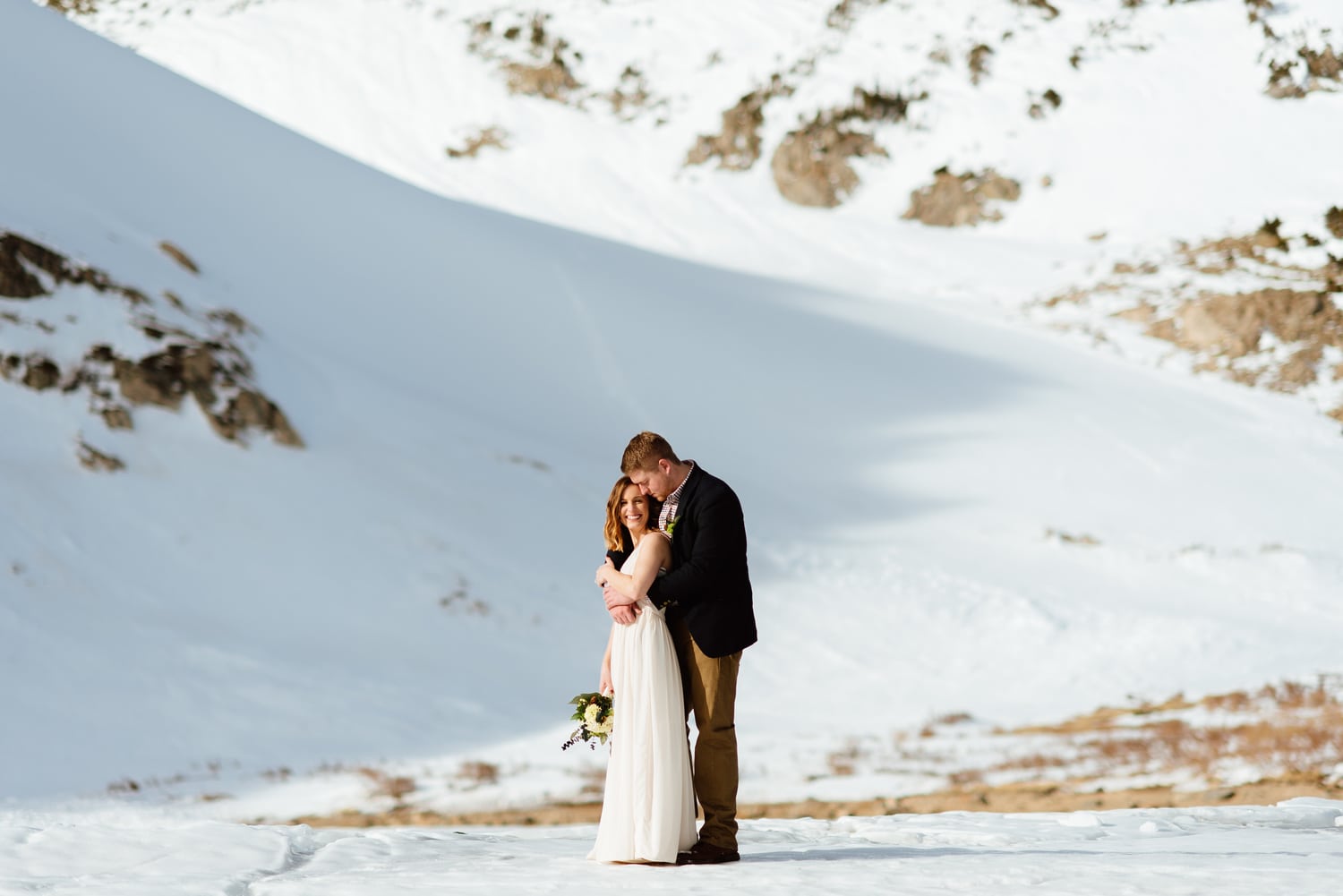 Bride and groom embrace, while standing in the snow, at St. Mary's Glacier in Idaho Springs, Colorado. 