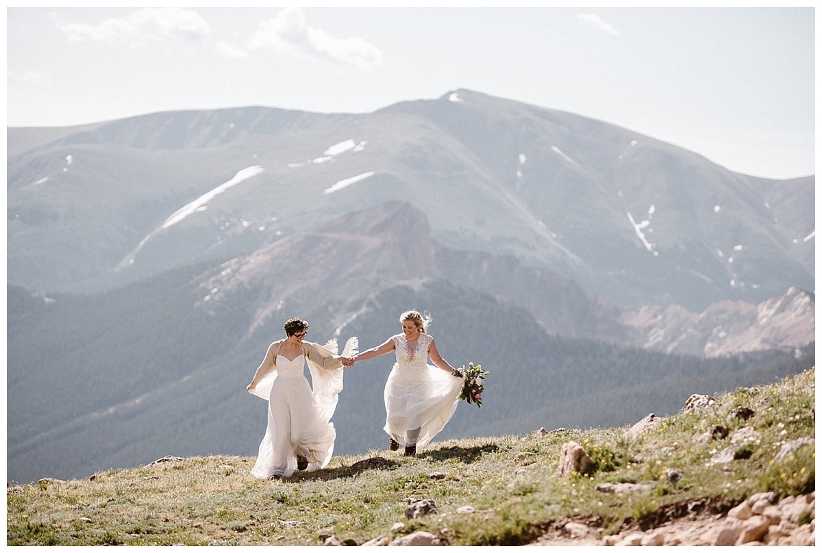 Two brides running while holding hands in Winter Park, Colorado. Their white dresses catch the sunlight and flow behind them. 