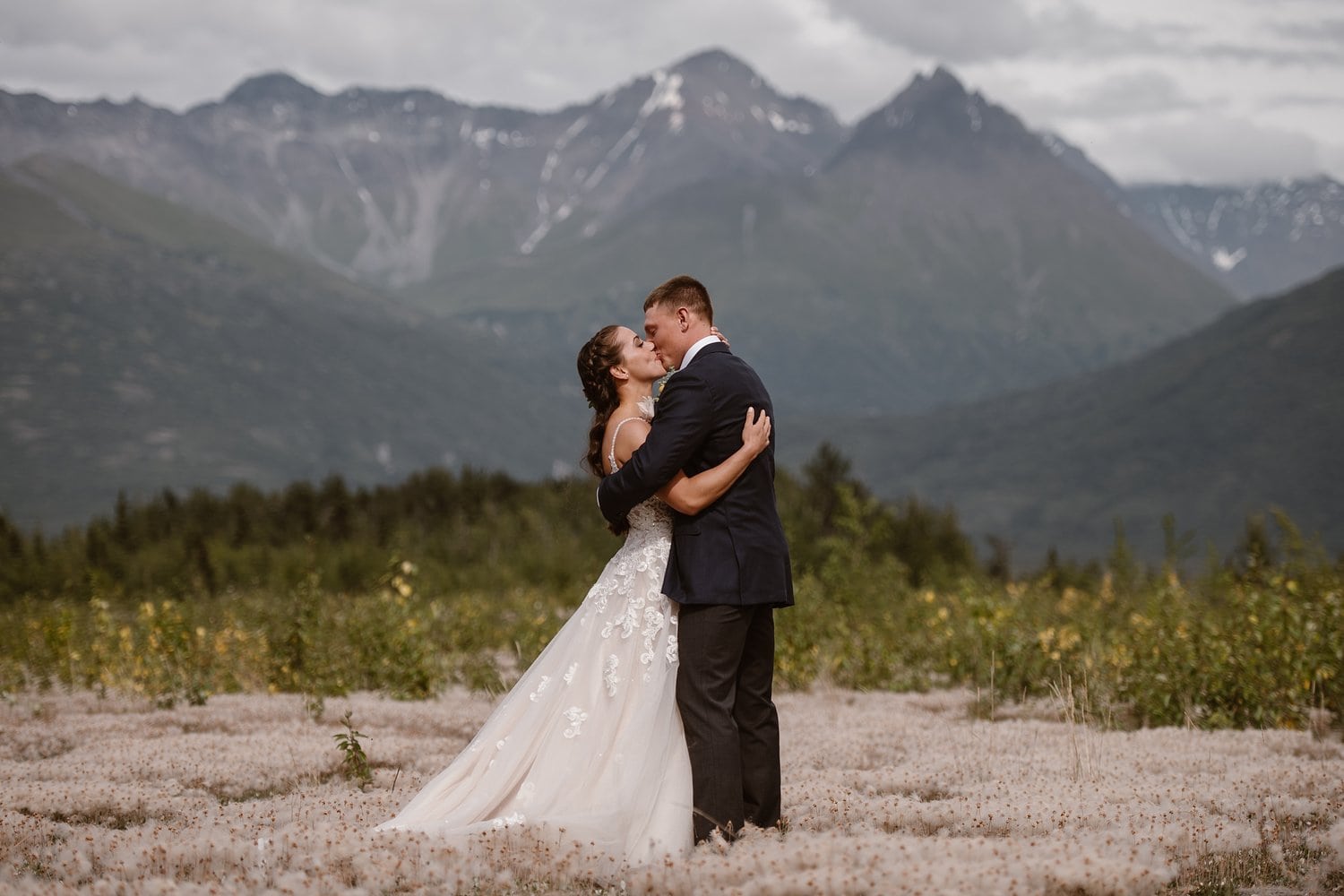 Bride and groom share a kiss on their elopement day in Alaska. There are mountains behind them. 