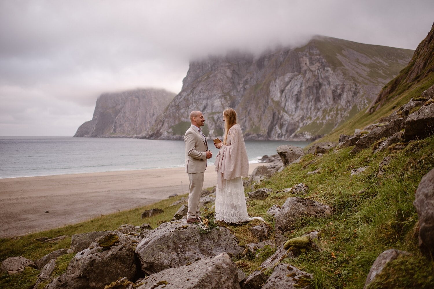 Bride reads her vows during their intimate elopement ceremony on a beach in Norway. There are mountains in the background. 