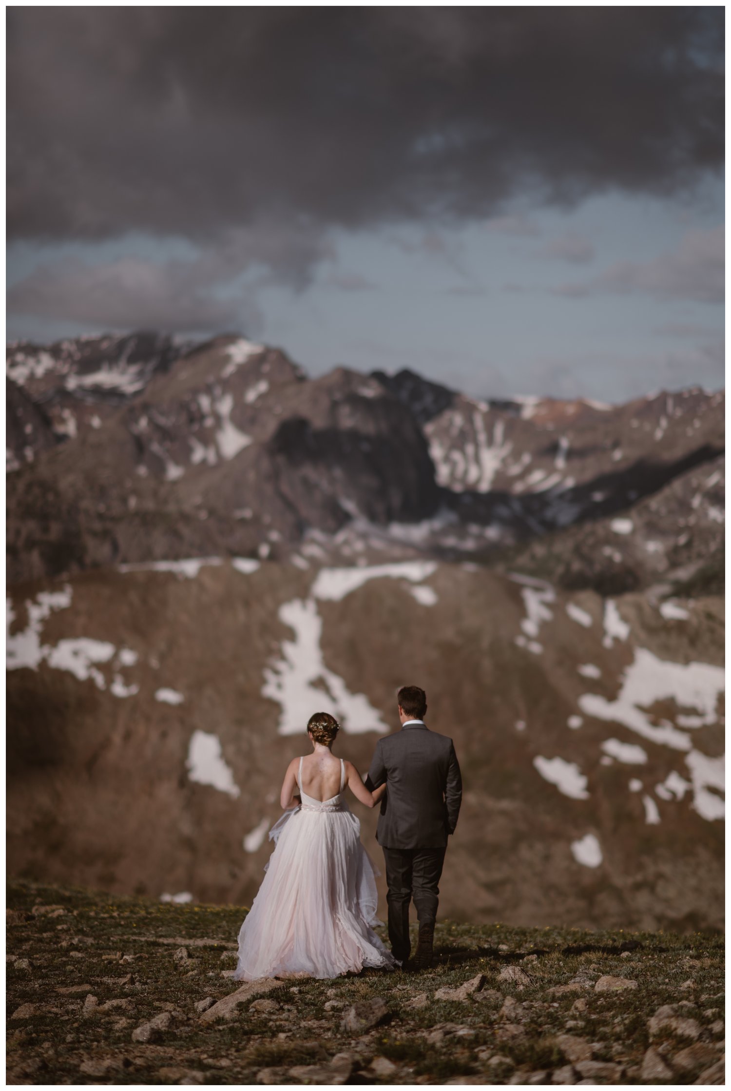 Bride and groom walk along a mountain ridge, while holding hands, during a sunrise hiking elopement near Aspen, Colorado. 