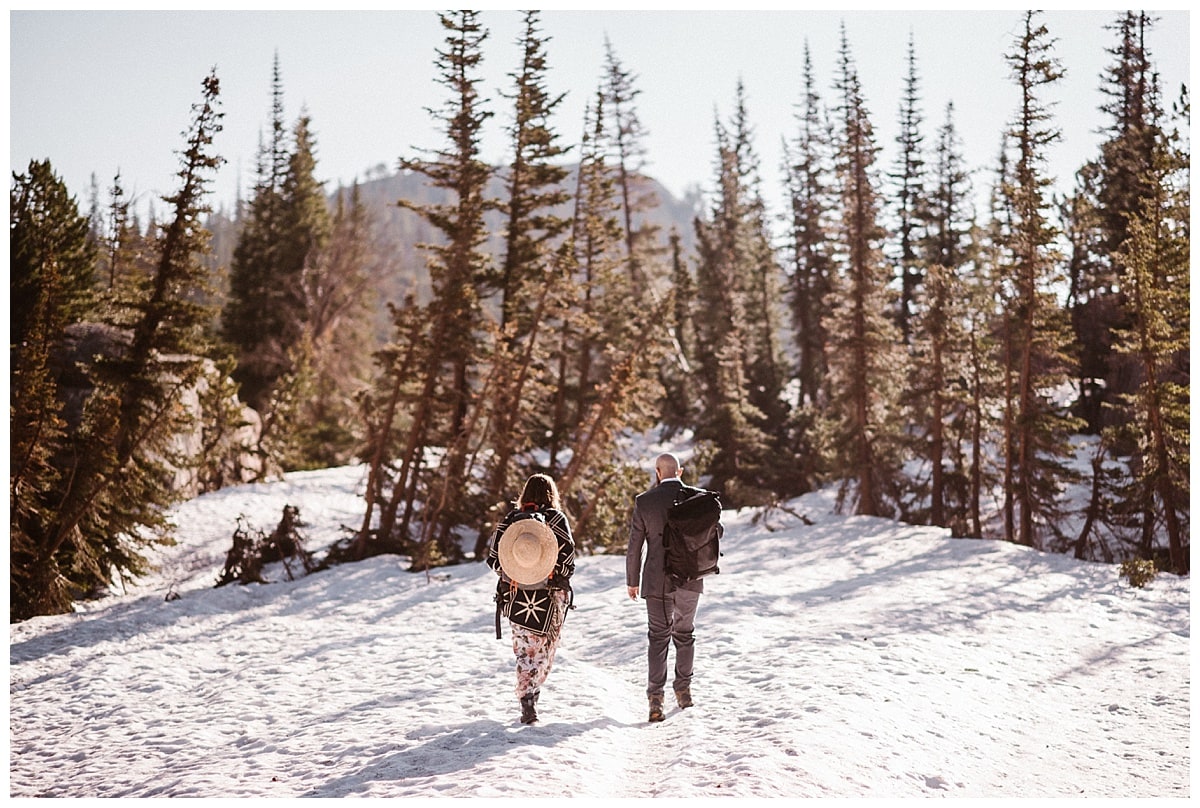 Bride and groom hike through snow in Rocky Mountain National Park. 