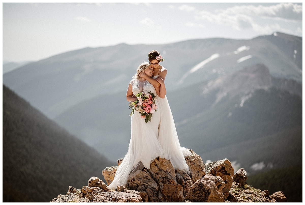 Two brides embrace, while standing on top of rocks in Winter Park, Colorado. 