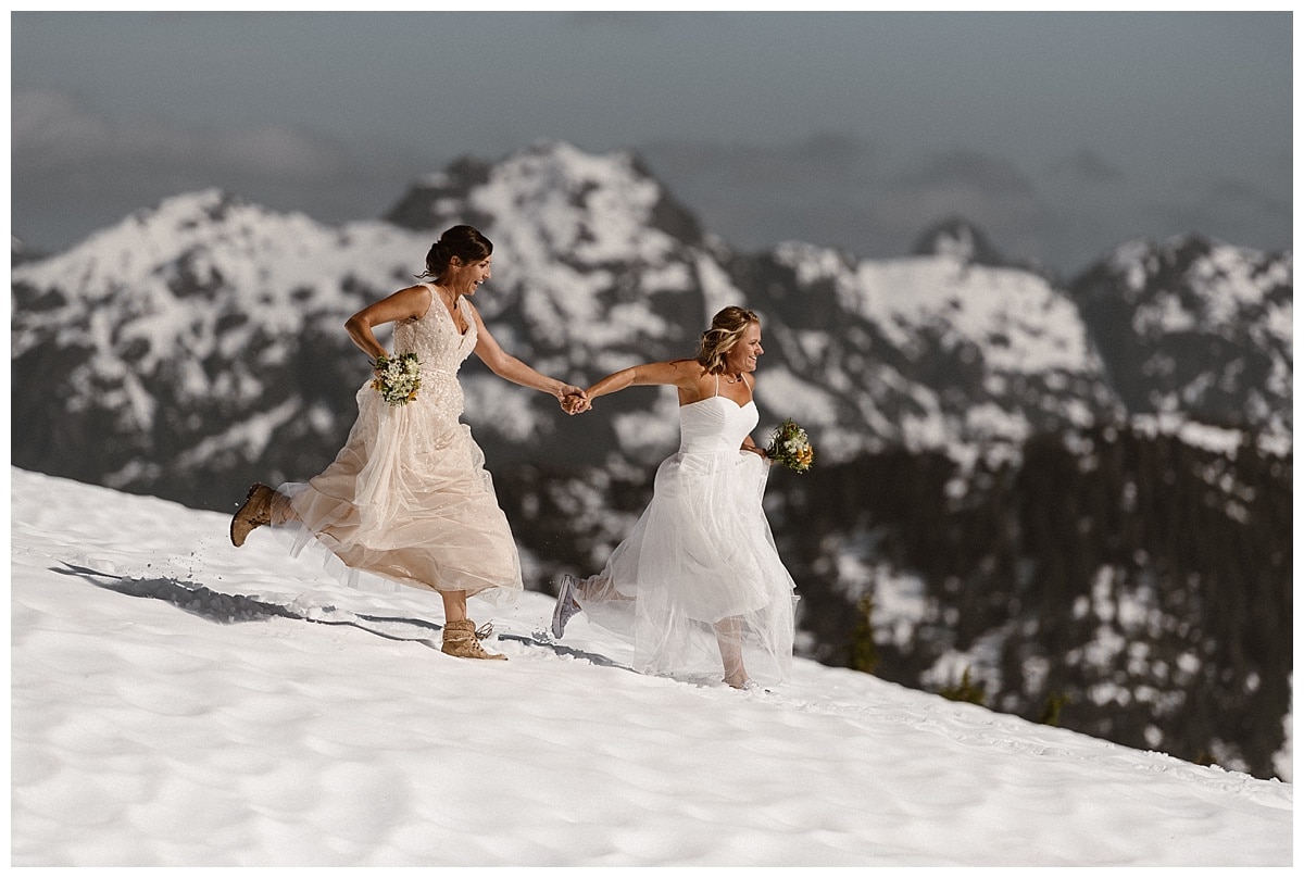 Two brides run through the snow holding hands on a glacial mountain in Tofino, Canada. 
