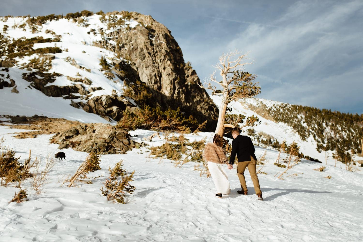 Bride and groom walking through snow, with mountains in the background, at St. Mary's Glacier in Idaho Springs, Colorado. 