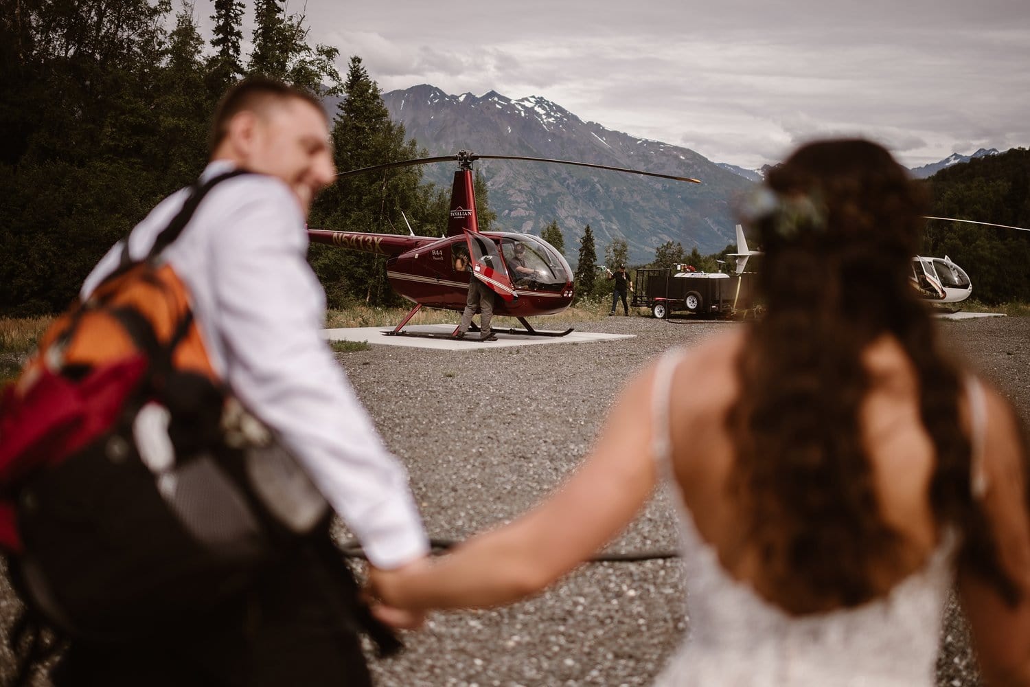 Bride and groom hold hands and walk towards helicopter.