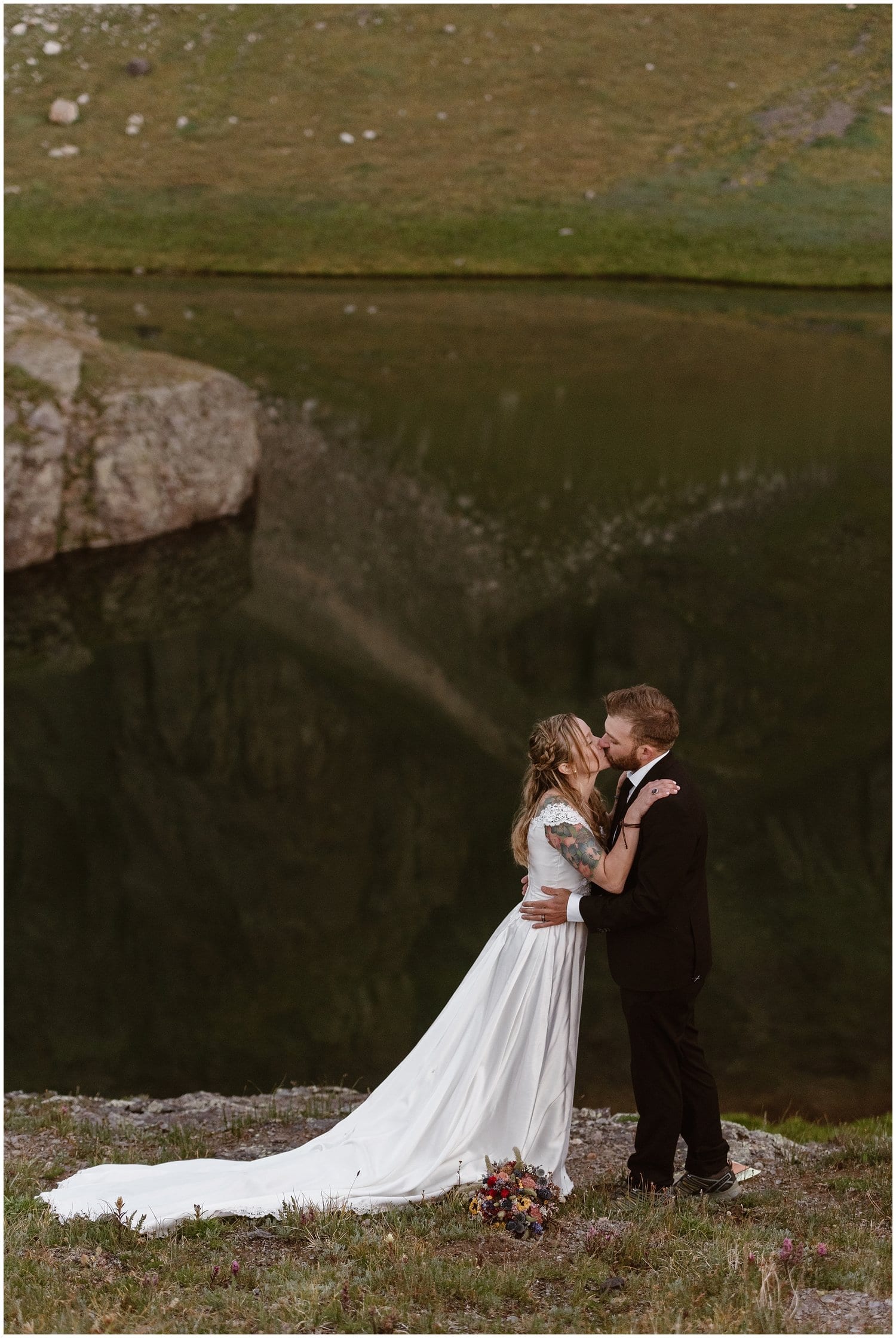 Bride and groom kiss in front of alpine lake in Ouray, Colorado. 