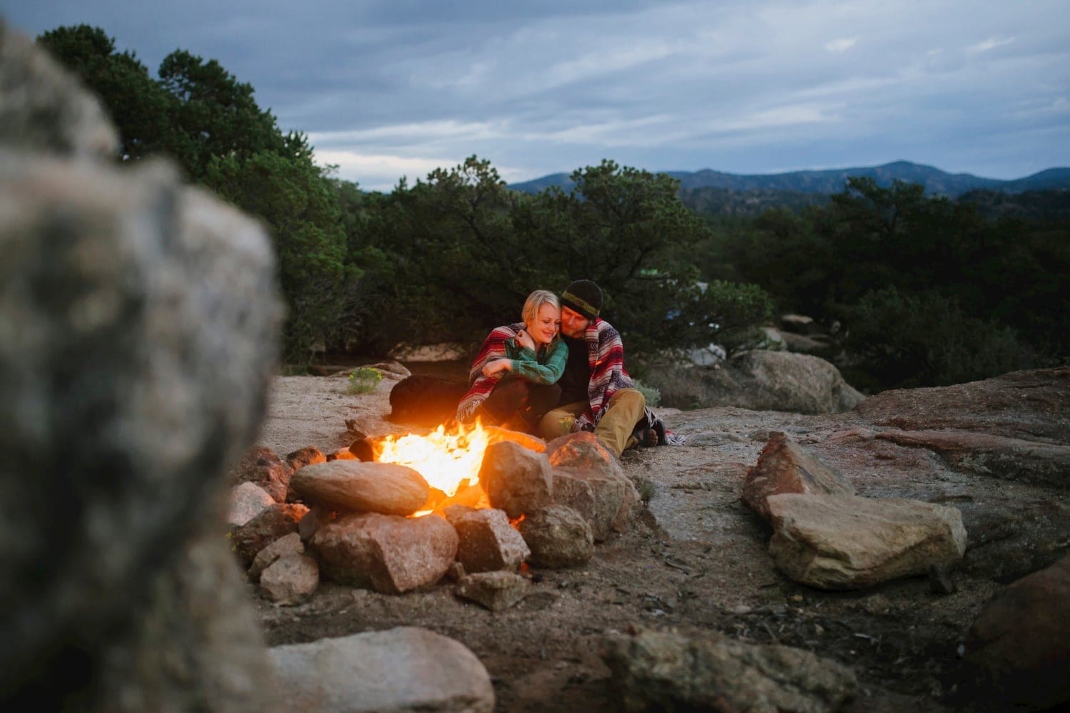 Couple celebrating their 10 year anniversary in Buena Vista, Colorado. They are sitting on a mountain, with a campfire in the foreground.