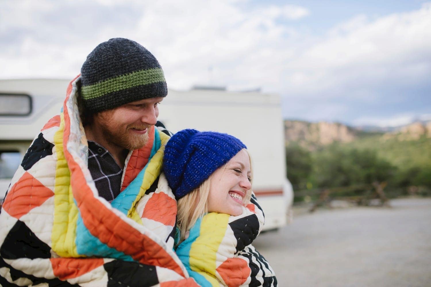 Couple wearing beanies, with a patterned blanket wrapped around them in Buena Vista, Colorado. Their RV is in the background. 