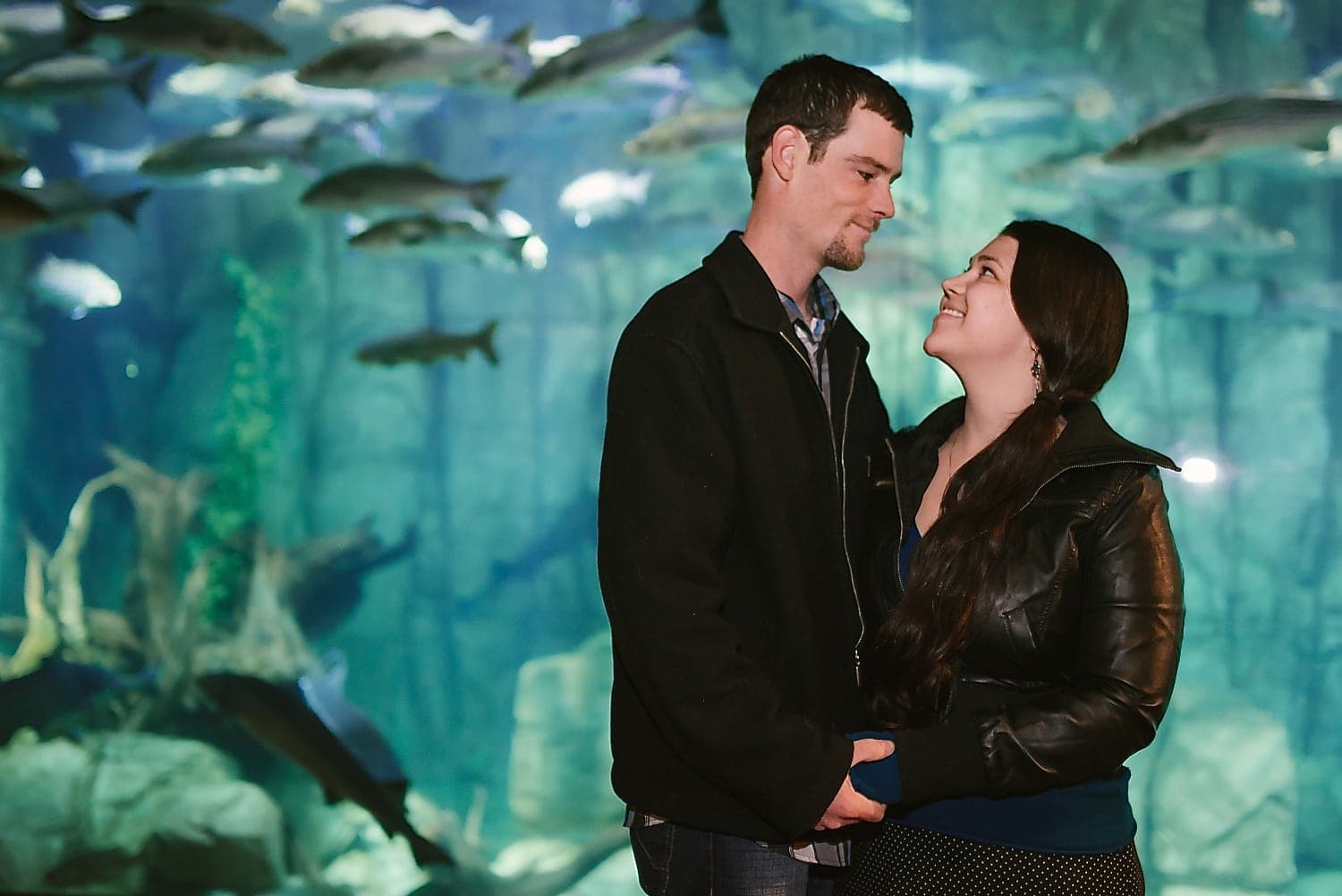 Couple holding hands and looking at each other, at the Denver aquarium. 