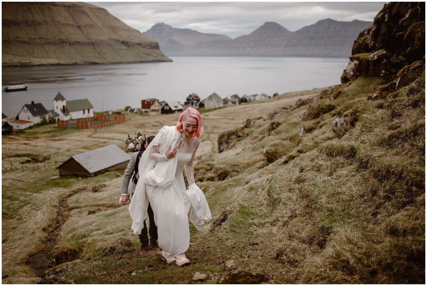 Bride and groom hike up hill in the Faroe Islands. 