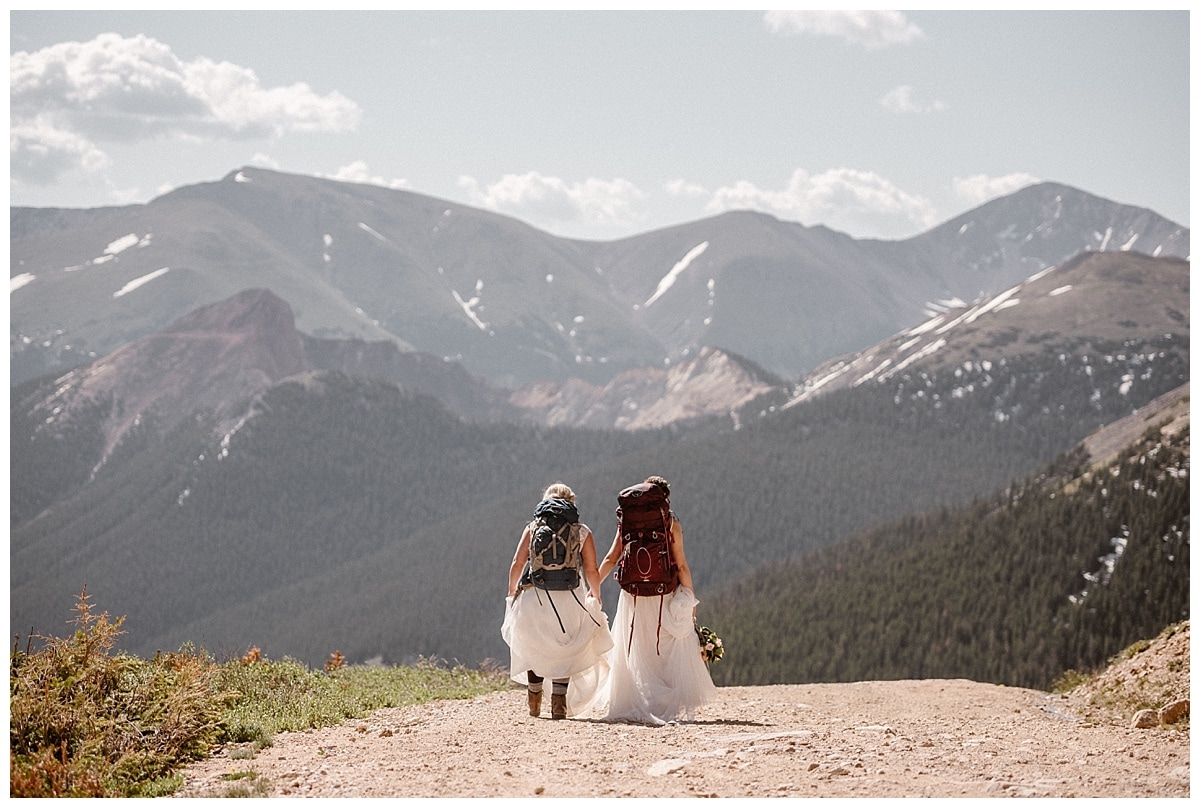Two brides hiking in Winter Park, Colorado. There are forests and mountains in the distance. 