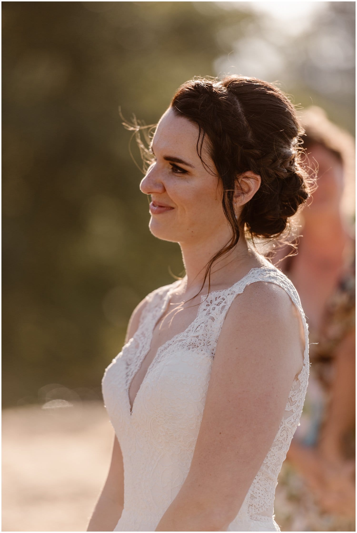 Bride is smiling with her hair in an updo and is wearing a white, lace wedding dress. 