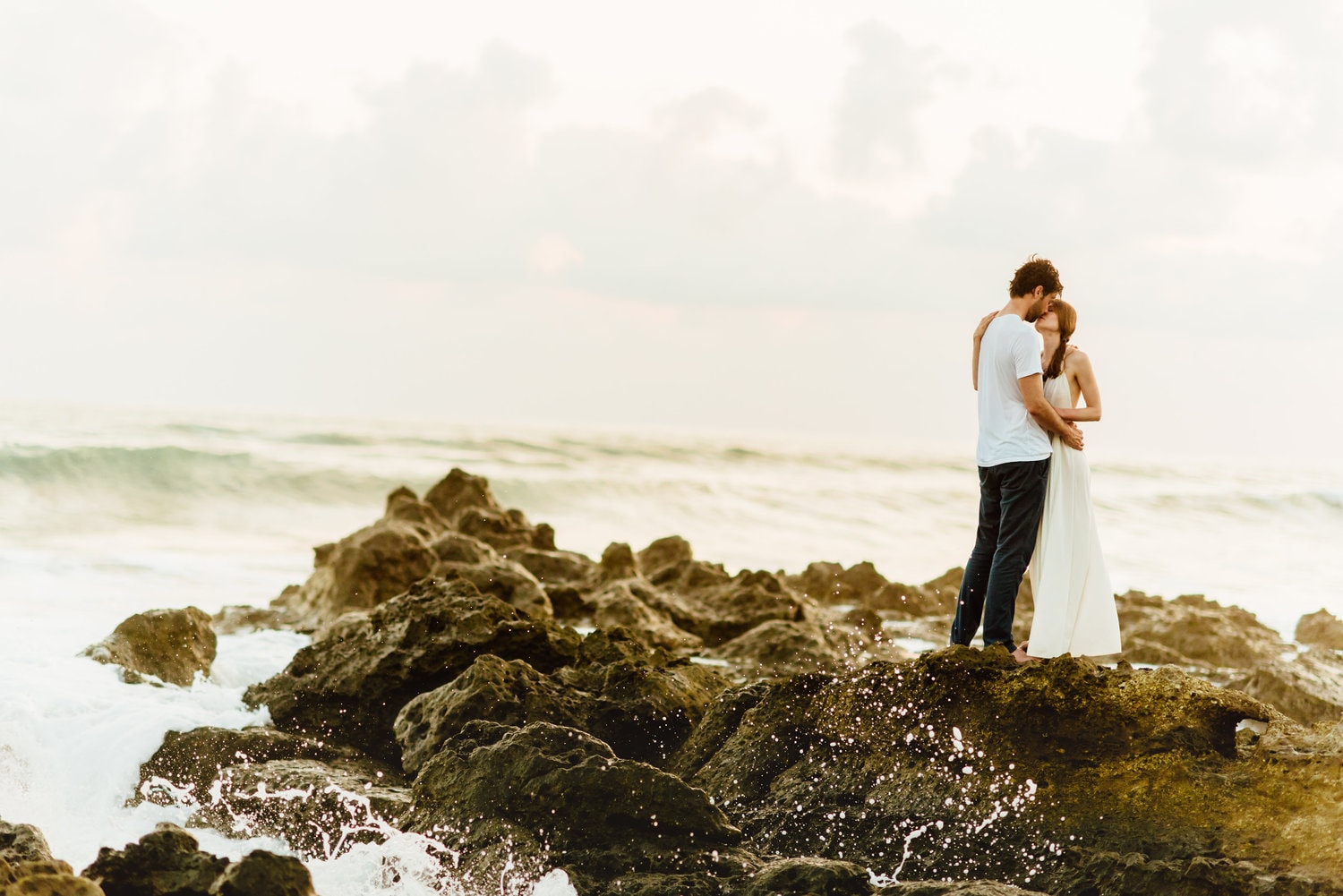 Bride and groom share a kiss while standing on rocks along the shore in Santa Teresa, Costa Rica.