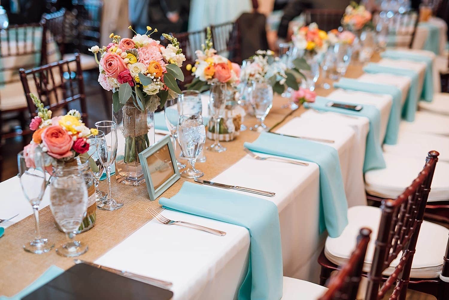 Table at bride and groom's ceremony decorated with a white table cloth, light blue linen, and floral arrangements in vases.