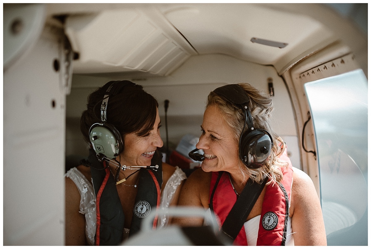 Two brides sitting in a helicopter and smiling at each other on their elopement day in Tofino, Canada. 