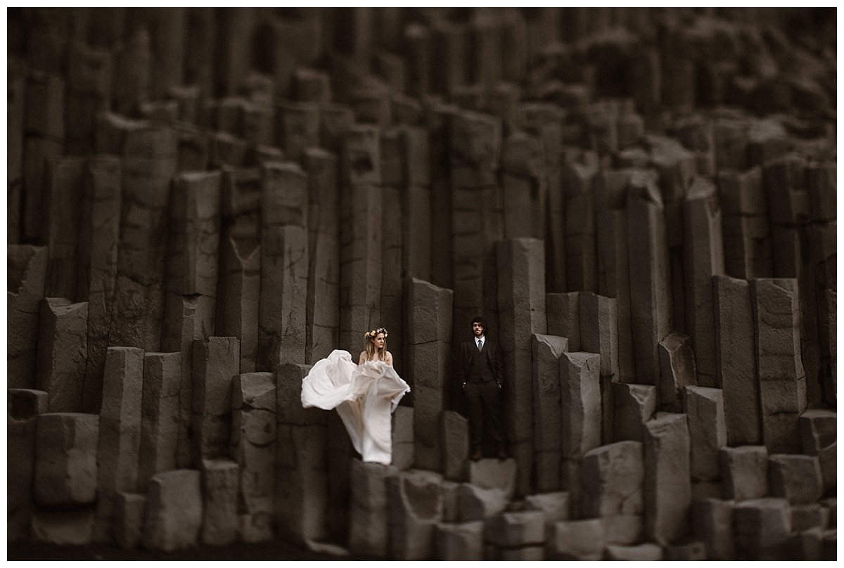 Bride and groom stand on grey rock formation in Iceland. 